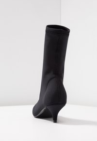 Černé kotníkové boty vyrobené z hladkého, pružného materiálu s elegantním siluetou, zúženým podpatkem, viditelným švem a minimalistickým designem.