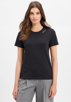 Czarny bawełniany t-shirt z okrągłym dekoltem, krótkimi rękawami, wyszywanym logo i małym wycięciem na dolnym brzegu. W połączeniu z jasnoszarymi spodniami.
