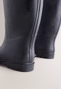 Schwarze Gummiregenstiefel mit glatter Oberfläche, ausgestattet mit erhabenen Nähten und einer strukturierten Sohle für besseren Halt. Robustes Design, geeignet für nasse Bedingungen.