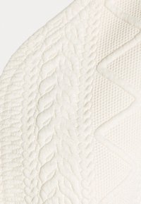 Gros plan d'un tissu tricoté de couleur crème avec des motifs torsadés et des losanges texturés.