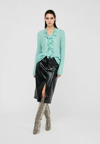 Šviesiai mėlyna dryžuota palaidinė su raukiniais priekyje, derinama su juoda odine midi sijonu su priekinės dalies plyšiu ir kelių ilgio auliniais su gyvatės raštu.