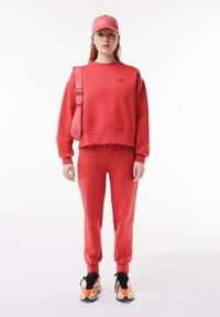 Röd sweatshirt och matchande joggers i mjukt material med avslappnad passform. En rosa keps fulländar outfiten, som kompletteras med flerfärgade sneakers.