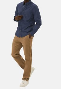 Camisa de botones azul marino con un bolsillo en el pecho, combinada con chinos marrón claro y zapatillas blancas, mostrando un corte relajado y un estilo casual.