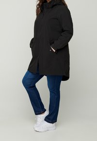 Czarny wodoodporny płaszcz z kapturem, przednim zamkiem błyskawicznym i kieszeniami. Połączony z niebieskimi dżinsami i białymi trampkami. Gładka tekstura, casualowy design.