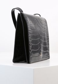 Borsa in pelle sintetica nera lucida effetto coccodrillo, dalla forma strutturata, con doppi manici e un dettaglio logo dorato sulla parte anteriore.