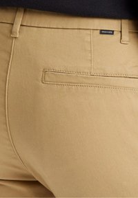 Pantalons en toile de coton beige avec une poche arrière plate. Le tissu est lisse avec une texture subtile.