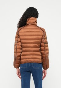 Jachetă puffer maro cu guler înalt, design matlasat și cusături contrastante negre. Include buzunare laterale cu fermoar și o siluetă ajustată.