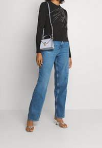 Schwarzer langärmeliger Pullover mit silbernen Verzierungen, blaue gerade Jeans, klare Absatzsandalen und eine kleine lavendelfarbene Handtasche.