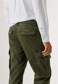 Olijfgroene cargobroek met opgestikte zakken, gemaakt van katoen. De achterkant heeft een gestructureerd oppervlak en verstevigde stikdetails.