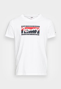 Hvid bomulds t-shirt med korte ærmer, der har et grafisk tryk i rød, sort og hvid med teksten "New York City Tommy Jeans Siden 1985."