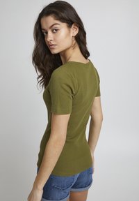 Olive rohelise ribaga T-särk lühikeste varrukatega, kehakujuline disain ja diskreetne ümmargune kaelus, koos teksashortsidega.
