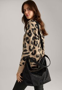 Borsa nera con una texture morbida, hardware dorato e una tracolla. La borsa presenta una chiusura a zip e dettagli decorativi sul tessuto.