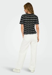 Stribet top med kort ærme i sort og hvid med et struktureret mønster, parret med højtaljede hvide bukser. Stoffet ser let ud.
