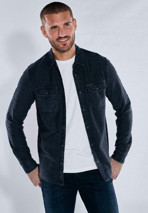 Dark blue button-up shirt with a textured stripe pattern, two front pockets, and long sleeves, worn over a white t-shirt.