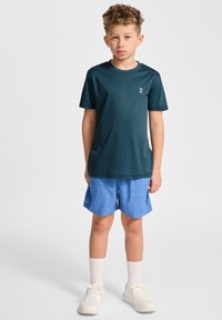 Teal kortärmad tröja med en liten grafik på bröstet, ihop med ljusblå shorts, vita strumpor och vita sneakers.