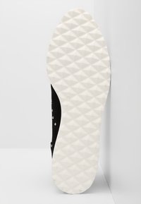 Zapato de ante negro con una suela de goma blanca texturizada que presenta un patrón de diamantes. Incluye adornos plateados en el lado. Talla marcada como 37.