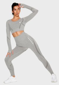 Gray athletic set featuring a cropped long-sleeve top and high-waisted leggings. Textured knit with reflective accents and logo detail.
