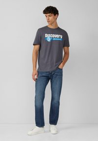 Grijze T-shirt met een "Discovery Channel"-afbeelding in wit en blauw, gecombineerd met blauwe spijkerbroek en witte sneakers. Eenvoudig ontwerp met ronde hals.