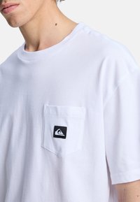 Hvid kortærmet t-shirt lavet af bomuld, med en brystlomme og et sort mærke-logo. Blød struktur med en afslappet pasform.