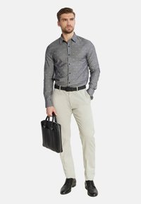 Camicia a righe grigia, pantaloni beige, cintura nera, scarpe nere e una valigetta nera. Abbigliamento casual da ufficio con una vestibilità strutturata.