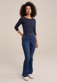 Marinblå långärmad tröja tillsammans med högmidjade mörkblå utsvängda jeans och vita sneakers. Bältet har en silverfärgad cirkulär spänne.