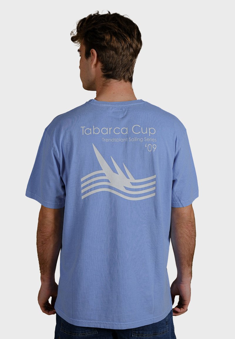 Ljusblå bomullströja med en vit grafisk design på baksidan med texten "Tabarca Cup" och vågor. Korta ärmar och rund halsringning.