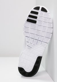 Semelle de chaussure de sport blanche avec une surface texturée, présentant un motif en grille et des sections accentuées noires. Matériau lisse avec un logo en relief.