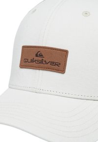 Weißer Stoffhut mit strukturiertem Finish, ausgestattet mit einem braunen Wildleder-Patch mit prägierter Logobeschriftung. Gebogener Schirm mit genähten Linien.
