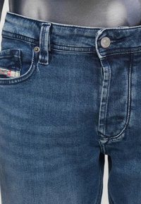 Τα τζιν από denim σε σκούρο μπλε πλύσιμο έχουν εφαρμοστή σχεδίαση με πέντε τσέπες, κούμπωμα με κουμπί και διακριτική ξεθώριαση στους μηρούς.