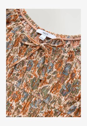 Top con patrón floral en tonos apagados de naranja, verde y azul. Con un escote fruncido, detalle de lazo y tejido texturizado. Etiqueta de la marca visible.