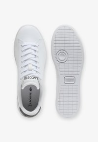 Sneakers bianche sintetiche con finitura liscia, design con lacci, interno imbottito grigio, suola in gomma testurizzata e logo Lacoste sulla linguetta.