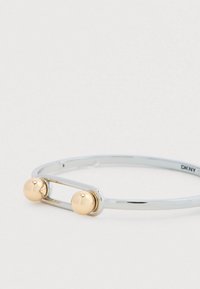 Brazalete de acero inoxidable plateado con dos acentos esféricos en tono dorado. Acabado liso, diseño abierto con una estética minimalista.