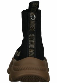 Czarny sneaker w stylu skarpetkowym z prążkowaną cholewką, beżową gumową podeszwą i złotymi akcentami z logo po bokach oraz na tylnej taśmie. Teksturowane detale na podeszwie.