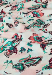 Bloemstof met een roze achtergrond, met ingewikkelde ontwerpen in rood, groen en zwart. Zachte textuur met opvallende details.