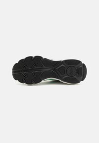 Schwarze Sportschuhsohle mit einem strukturierten Gummimuster. Auffällige Rillen für Griffigkeit und ein kreisförmiges Logo in der Mitte.