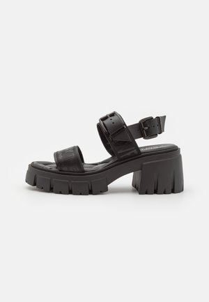 Zwarte platform sandalen met brede banden en een dikke hak. Gemaakt van glad synthetisch materiaal met een gestructureerd detail en een verstelbare gesp.