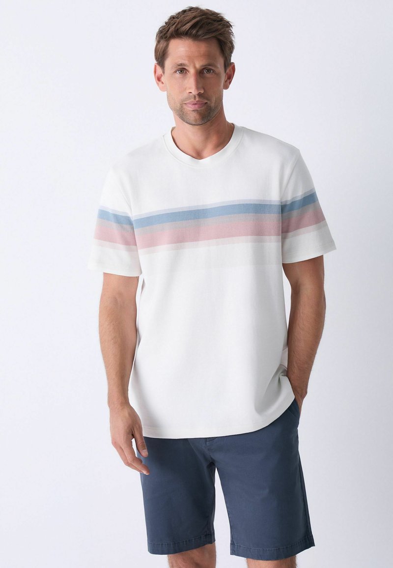 T-shirt en coton blanc avec des rayures horizontales bleues et roses. Manches courtes, col rond, associée à un short marine.