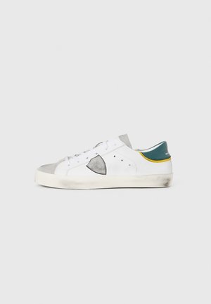Lage sneakers van wit leer met grijze suède accenten, voorzien van een groene hiel tab en gele afwerking. Rubberen zool met lichte slijtage.