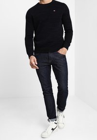 Svart stickad tröja med rund hals, kombinerad med mörkblå slim-fit jeans och vita sneakers med svarta detaljer.