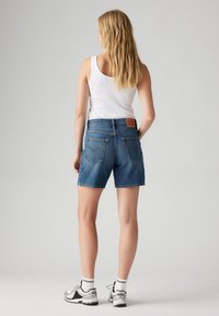 Szorty dżinsowe w średnim odcieniu niebieskiego z prostym krojem, widocznym przeszyciem oraz dwoma tylnymi kieszeniami. Noszone z białym topem na ramiączkach i sportowymi butami.