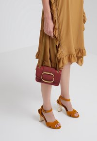 Röd läderhandväska med ett guldspänne, kombinerad med en senapsfärgad klänning med volanger och gula mocka blockklackssandaletter med genomskinlig klack.