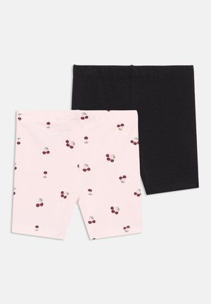 Deux paires de shorts pour enfants, l'une unie noire et l'autre rose clair avec de petits motifs de cerises rouges, posées à plat sur un fond blanc.