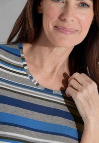 Gestreepte top met blauwe, grijze en zwarte horizontale lijnen. Zachte stof met een ronde halslijn. Close-up van de halslijn en schouder, hand die de stof aanraakt.