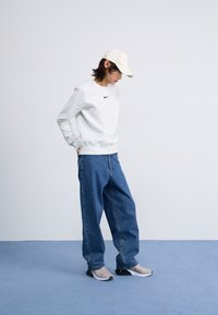 Szürke pulóver fekete Nike logóval, laza kék farmernadrág és világosbarna sapka. A szürke és fekete sportcipők teszik teljessé az öltözéket.