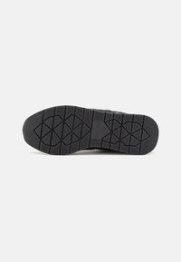 Semelle de chaussure en caoutchouc noir avec un motif de grip texturé, comportant des formes hexagonales et triangulaires pour l'adhérence. Design minimaliste, sans aucune marque visible.