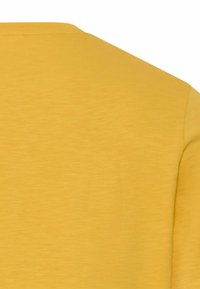 Solider senfgelber Stoff eines kurzärmeligen Hemds mit Fokus auf den oberen Rücken- und Schulterbereich mit sichtbaren Nähten.