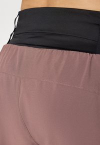 High-waisted athletic leggings featuring a black waistband and soft, smooth mauve fabric with subtle stitching details.