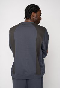 Hanorac de culoare gri închis cu accente contrastante pe panouri, manșete și tiv striate, cu un finisaj texturat și detaliu cu logo pe partea din spate.