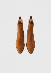 Brązowe zamszowe botki za kostkę z wąskim noskiem, niskim obcasem i elastycznymi panelami bocznymi. Projekt zawiera krótki uchwyt z tyłu.