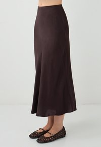 Jupe midi en satin marron foncé avec une texture lisse, une forme évasée et une taille haute, associée à des ballerines tressées marron.